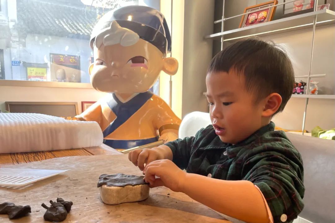 江苏无锡南长街NANIMOMO咖啡馆内，一名儿童在父母带领下体验制作惠山泥人 。（朱国亮 摄）